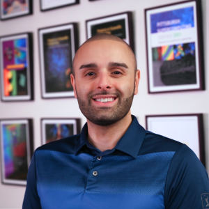 A man with medium-light skin tone and brown hair smiles at the camera.