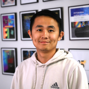 A man with medium-light skin tone and black hair smiles at the camera.