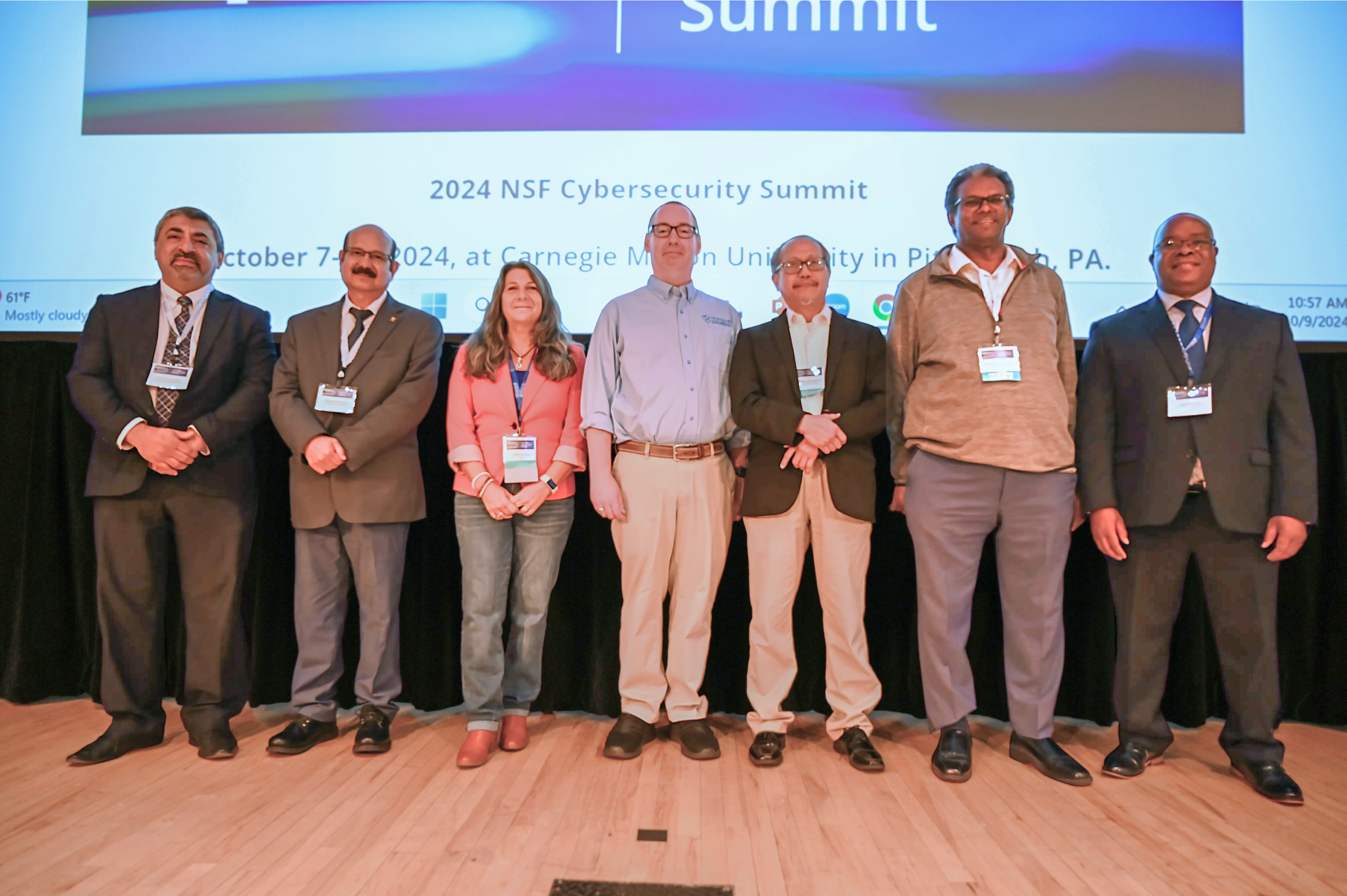 A group of people stand on a stage for a group picture at the Summit.