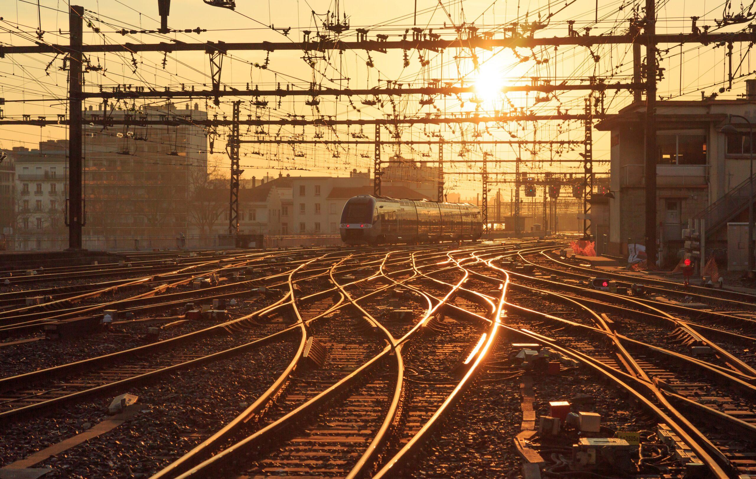 The tracks of a train station are illuminated by a sunset.